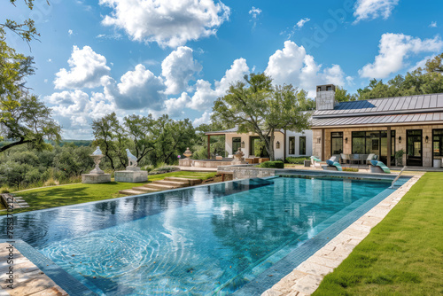 A large  beautiful pool in the backyard of an elegant Texas ranch home with green trees and blue sky.