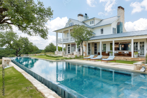 A large  beautiful pool in the backyard of an elegant Texas ranch home with green trees and blue sky.