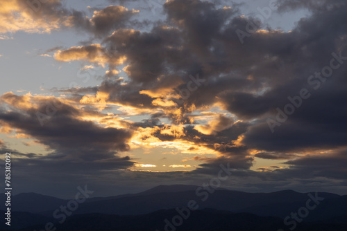 Sunset over a layered mountain range with dramatic dark clouds rimmed in orange light, beautiful landscape scene, horizontal aspect
