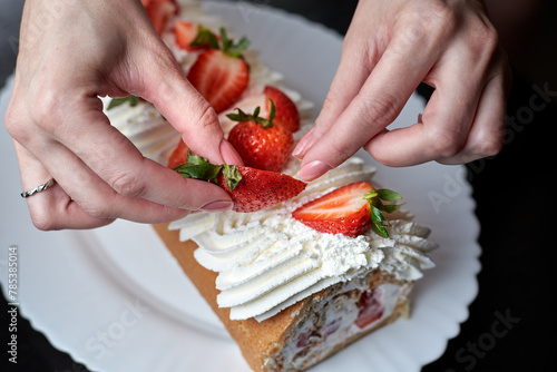 girl decorates a cream roll with fresh strawberries

