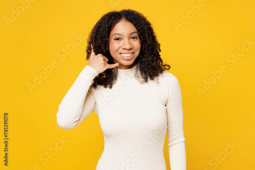 Little kid teen girl of African American ethnicity wear white casual clothes doing phone gesture like says call me back isolated on plain yellow background studio portrait Childhood lifestyle concept photo