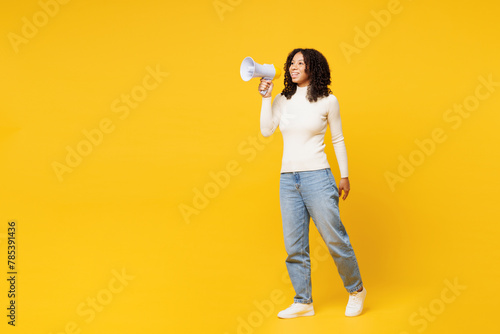Full body little kid teen girl of African American ethnicity wear white casual clothes hold megaphone scream announces discounts sale Hurry up isolated on plain yellow background. Childhood concept.