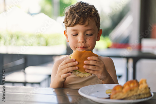 Little Boy Eating Sandwich and French Fries at Table photo