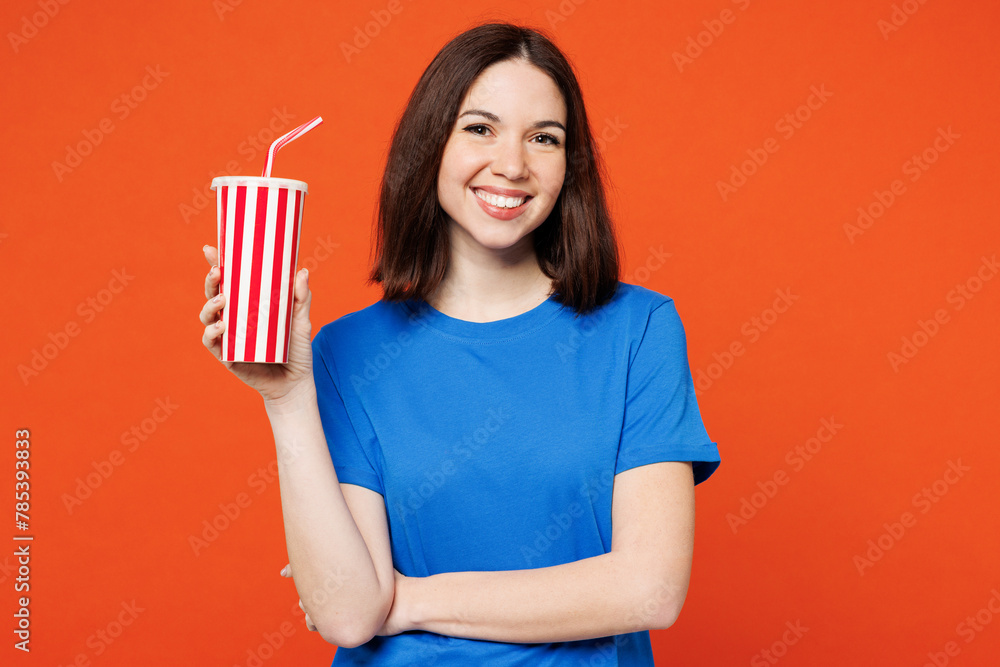 Young smiling fun happy woman she wear blue t-shirt casual clothes hold in hand cup of soda pop cola fizzy water look camera isolated on plain red orange background studio portrait. Lifestyle concept. Young smiling fun happy woman she wear blue t-shirt casual clothes hold in hand cup of soda pop cola fizzy water look camera isolated on plain red orange background studio portrait. Lifestyle concept.