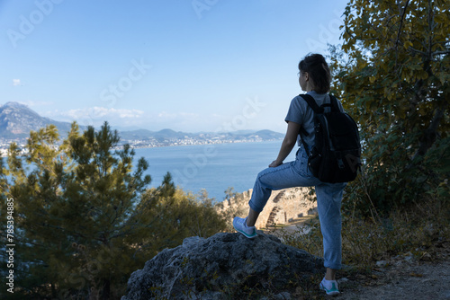  young girl tourist stands on a mountain path and looks down at a sea bay. selective focus . High quality photo