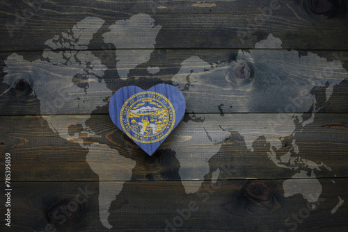 wooden heart with national flag of nebraska state near world map on the wooden background.