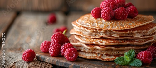 A neat stack of pancakes with vibrant fresh raspberries on top, creating a visually appealing breakfast or brunch dish.