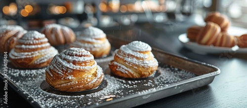 A selection of fresh pastries, sprinkled with powdered sugar, arranged neatly on a tray placed on top of a wooden table. photo