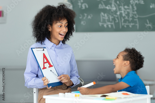 Cheerful black female speech therapist and little boy learning and pronouncing letters during lesson in office photo