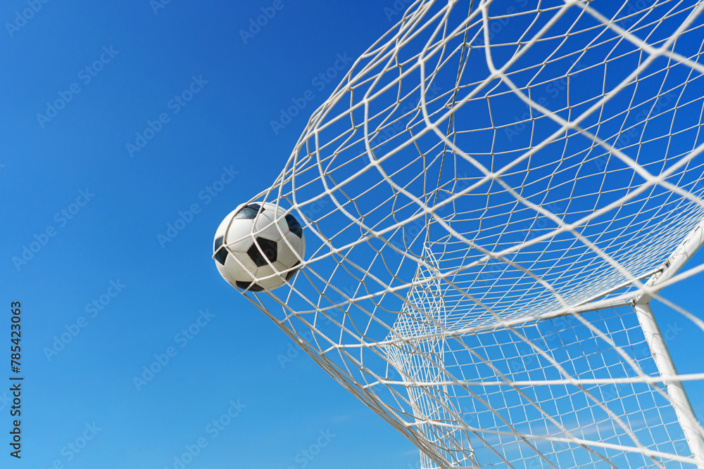  Soccer ball in soccer goal net in a big stadium isolated on blue sky. soccer net. - obrazy, fototapety, plakaty 
