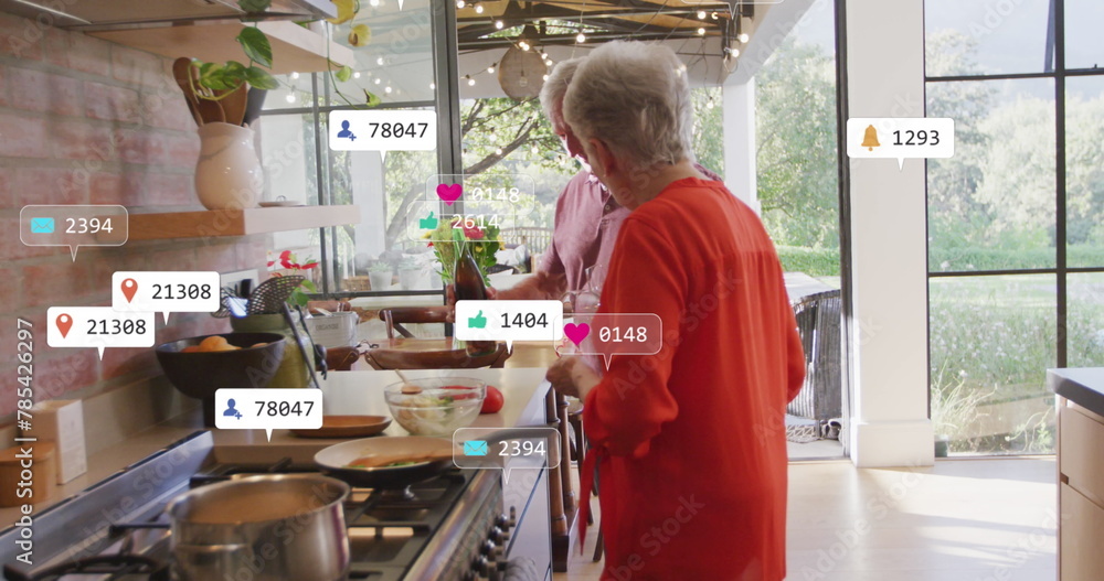 Image of social media text and icons over senior caucasian couple in kitchen at home