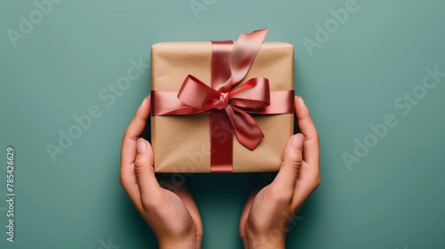 Hands of woman holding a beautifully wrapped gift with red ribbon on green background for special occasion or celebration concept