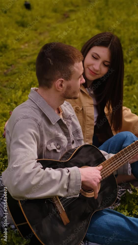 Young couple picnicking in the forest. Man playing guitar, teenage love and friendship, first date, young tourists enjoying outdoor activities. Young couple picnicking in the forest. Man playing guitar, teenage love and friendship, first date, young tourists enjoying outdoor activities.