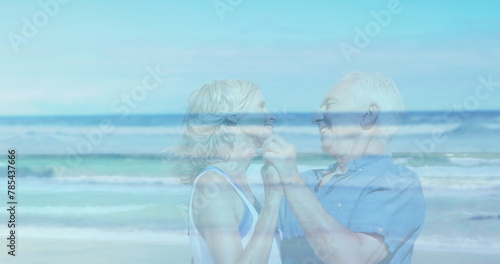 Image of landscape with ocean over happy senior caucasian couple dancing at beach