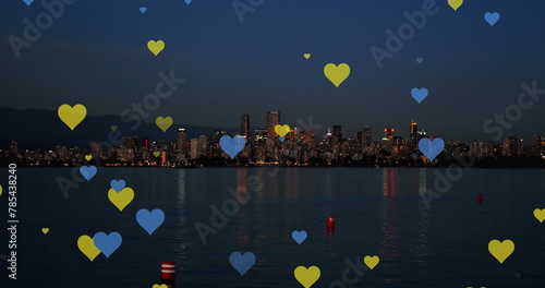 Image of yellow and blue hearts floating over night cityscape
