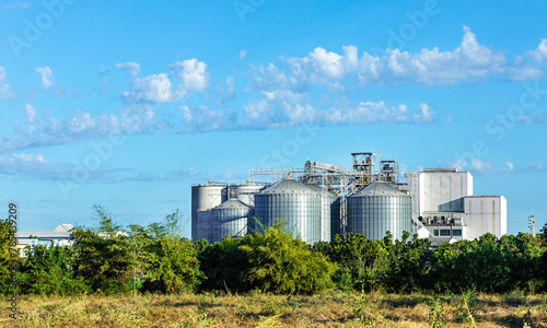 Silver silos on agro manufacturing plant for processing drying cleaning and storage of agricultural products, flour, cereals and grain. Agricultural, processing plants