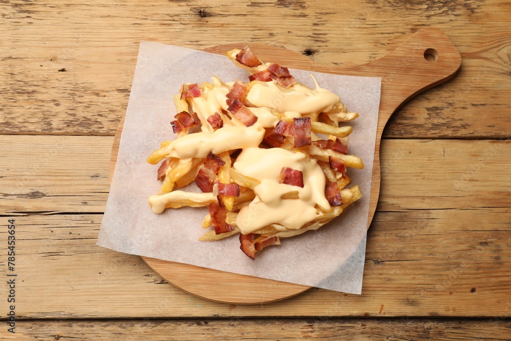 Delicious French fries with bacon and cheese sauce on wooden table, top view