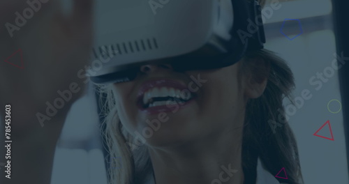 Image of multicolored geometric shapes over smiling caucasian businesswoman using vr headset