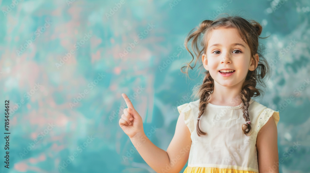 little happy child points with his index finger at something on a light blue wall, space for text