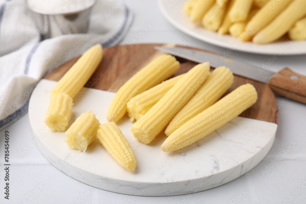 Tasty fresh yellow baby corns and knife on white tiled table, closeup Tasty fresh yellow baby corns and knife on white tiled table, closeup