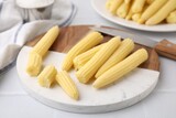 Tasty fresh yellow baby corns and knife on white tiled table, closeup