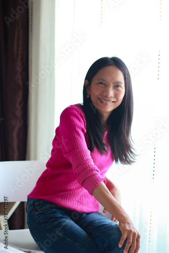 Asian woman sitting on the bed at home and smile at camera, women smile, pink silk shirt.