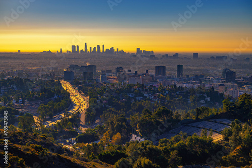 Hollywood downtown at sunrise with Los Angeles skyline in the background and traffic on US-101 highway in the foreground.