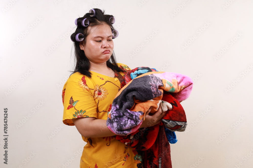 Fototapeta premium Tired unhappy asian housekeeper woman standing while holding clothes