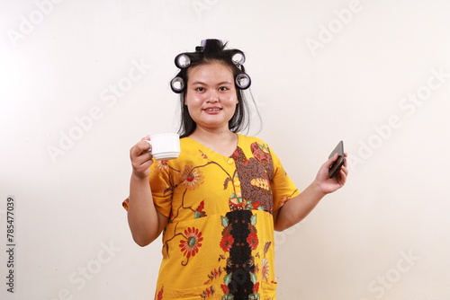 Happy Relaxed asian housekeeper woman standing holding a cup of coffee while carrying cell phone