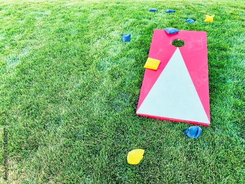 Red and white cornhole board with bean bags on lawn in summer, leisure game activity