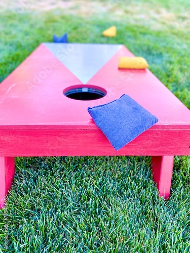 Red and white cornhole board with bean bags on lawn in summer, leisure game activity