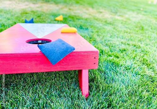 Red and white cornhole board with bean bags on lawn in summer, leisure game activity