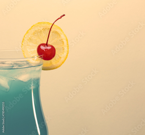 Classic blue lagoon cocktail garnished with lemon slice and cherry on warm beige background with copy space. Vintage style.