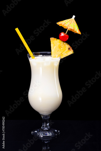 Pina colada drink with straw, slice of pineapple, maraschino cherry and cocktail umbrella isolated on black background.