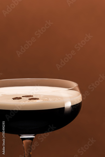 Espresso Martini cocktail served in fancy elegant coupe glass garnished with coffee beans on coffe color background.