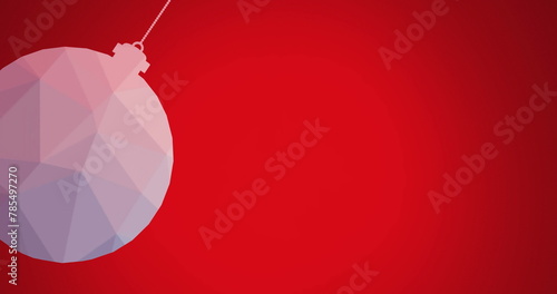 Image of close up of hanging bauble swinging against red background
