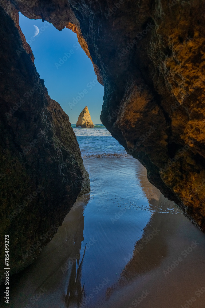 3 brothers beach with islet and moon seen through a rock in the town of Alvor in the Algarve region