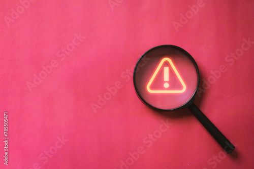 Glowing red triangle caution warning or exclamation sign inside magnifier glass for notification error and maintenance concept. © Dilok