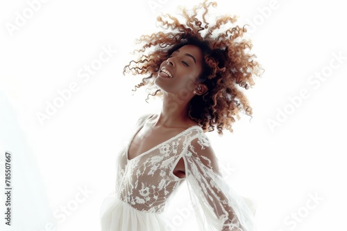 Attractive black woman with long curly hair laughing, wearing brown against a white background, in a studio photography setting with soft lighting