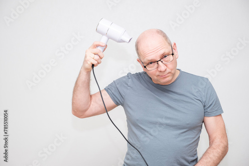 Bald Caucasian man uses a hair dryer.