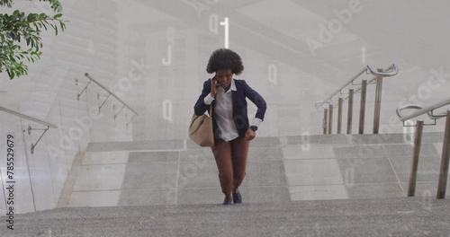 Image of numbers over african american businesswoman talking on smartphone while climbing stairs