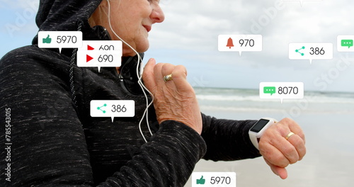 Image of notification bars over senior caucasian woman with headphone using smartwatch at beach
