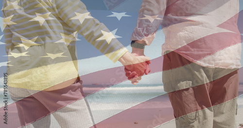 Image of senior caucasian couple holding hands on beach over flag of united states of america