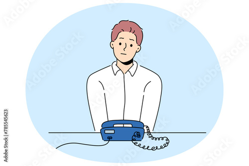 Unhappy man sit at desk look at landline phone waiting for someone call. Frustrated guy awaiting ring looking at corded telephone. Vector illustration.