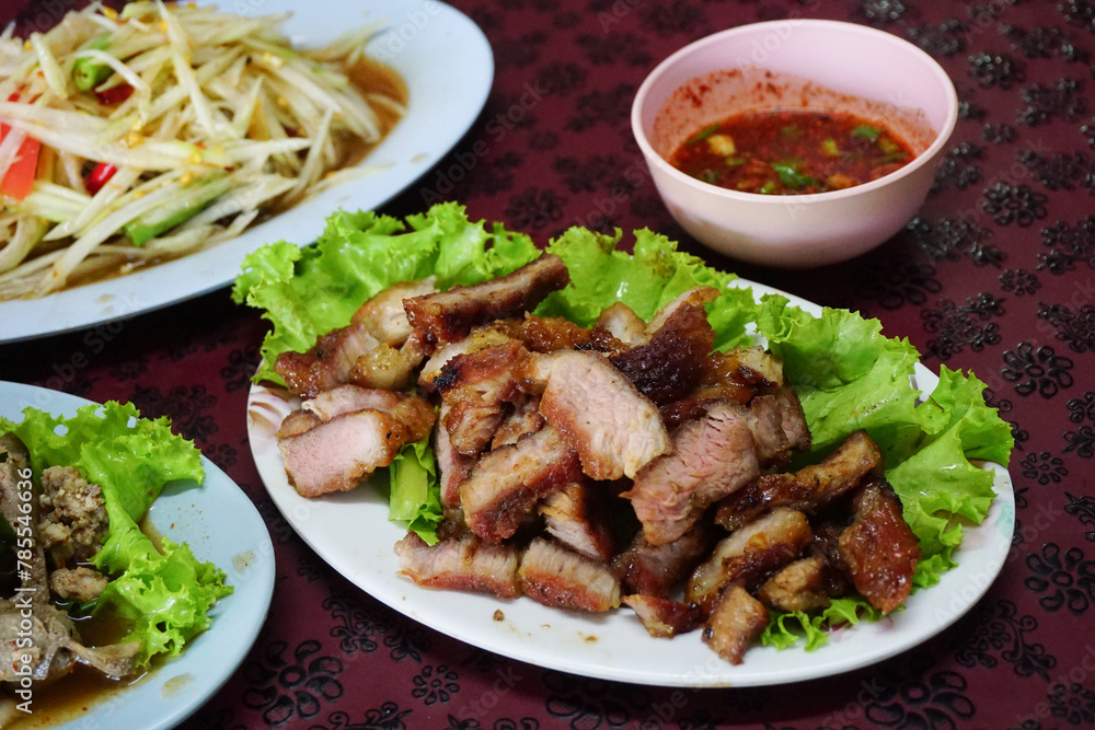 Grilled Pork Neck in Thai style, on white dish and other food on table
