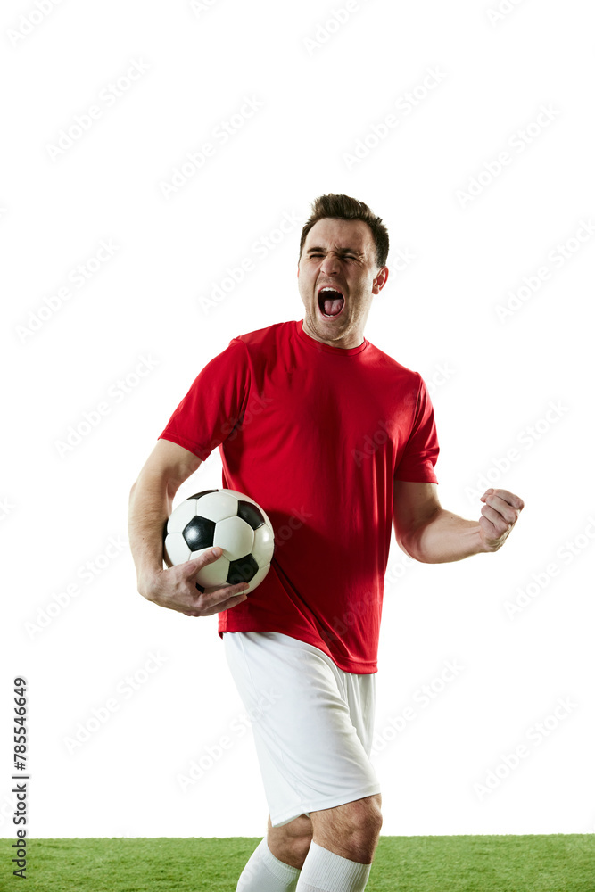 Obraz premium Emotive football player in red t-shirt and white shorts standing with ball on field and shouting isolated on white background. Concept of professional sport, game, competition, tournament, action