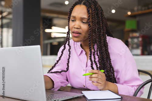Young biracial woman with long braided hair working on laptop in a modern business office