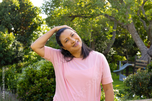 Mature biracial woman standing outside, stretching neck and smiling at home