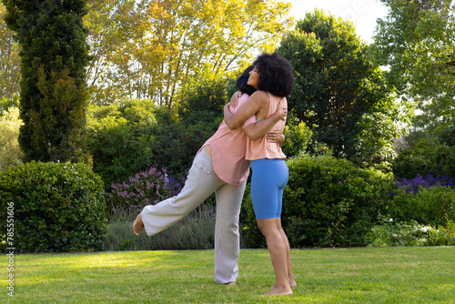 Mature biracial woman hugging young adult daughter in garden at home