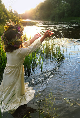 girl in flower wreath stand in river. summer nature background. Floral crown, symbol of summer solstice. ceremony for Midsummer, wiccan Litha sabbat. pagan folk holiday Ivan Kupala